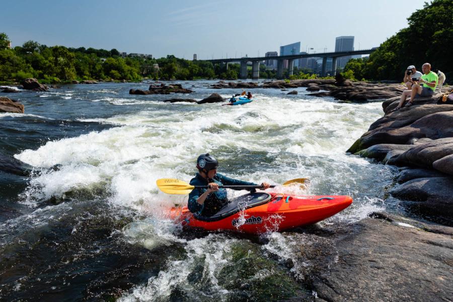 A kayaker running whitewater rapids on the James River with the city skyline beyond